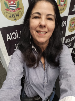 Mulher sorridente tirando uma selfie com um painel ao fundo com a logotipo de Policia Civil 