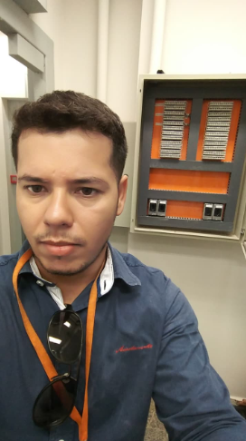 Selfie de um homem trabalhando e uma caixa elétrica ao fundo. 