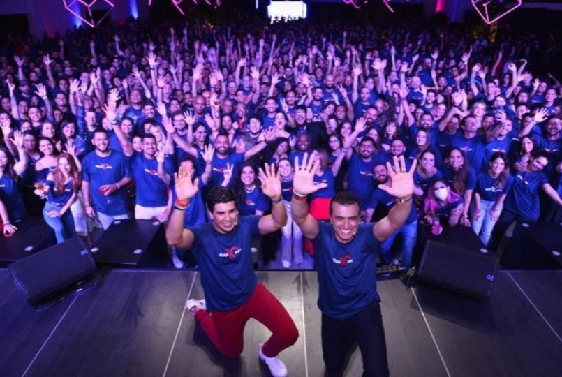 Dois homens ajoelhados na frente do palco acenando, com uma grande multidão com as mãos para o alto ao fundo