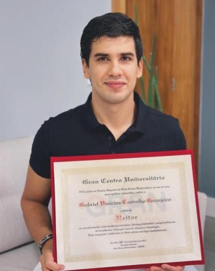 Homem sorridente segurando um diploma emoldurado com a inscrição 'Gran Centro Universitário'