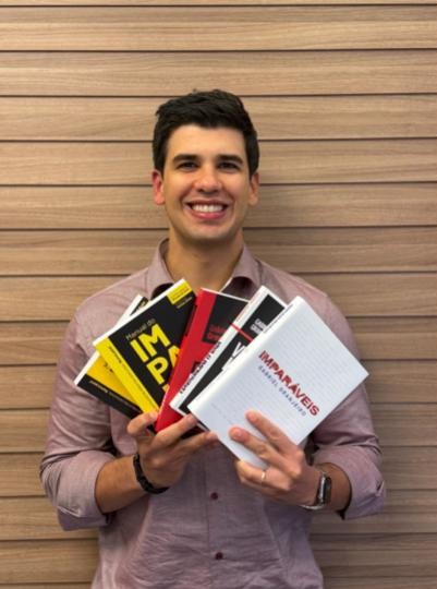 Homem sorridente segurando diversos livros nas mãos