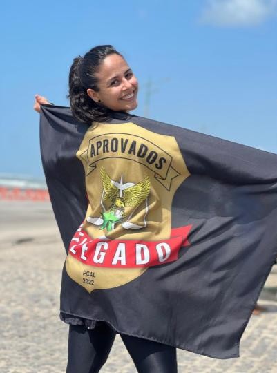 Mulher sorridente tirando foto com uma bandeira escrito "Aprovados" e um brasão escrito "Delegado".