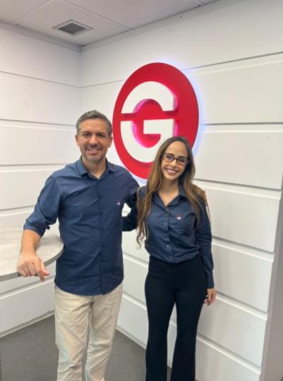 Mulher sorridente ao lado de um homem com a logotipo do Gran ao fundo. 