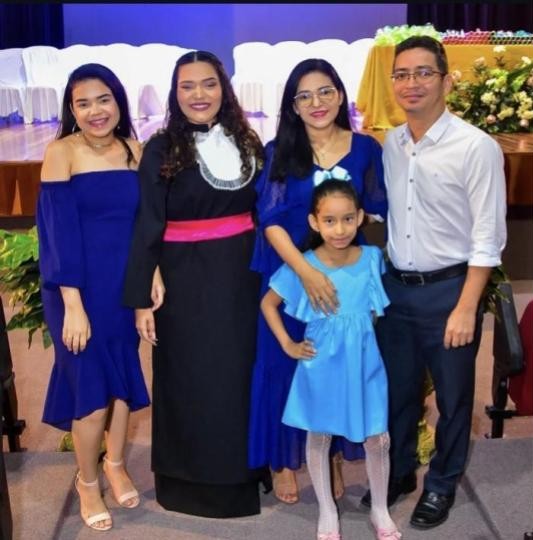 Foto em família de um casal com três filhas em uma formatura, todos sorridentes.